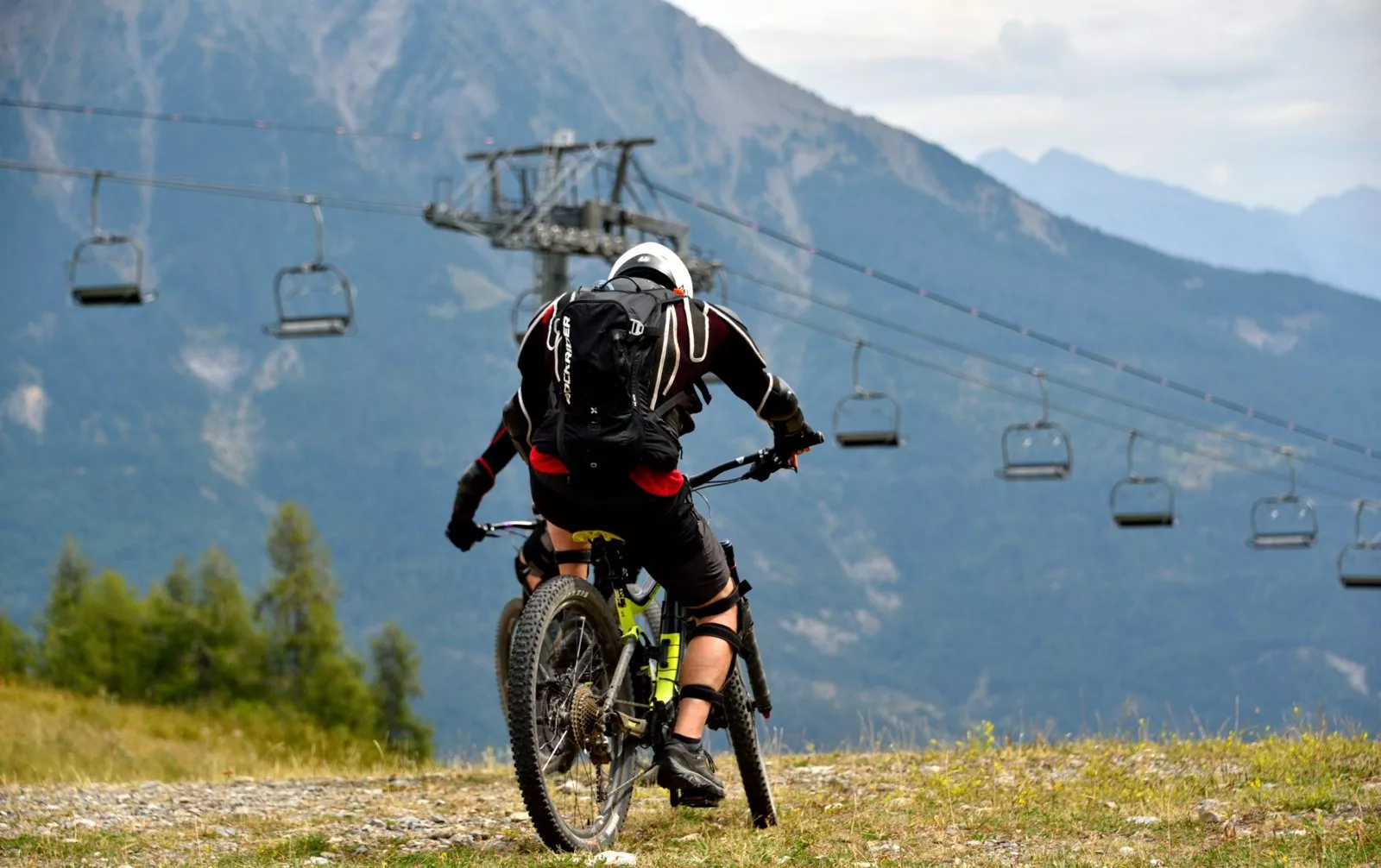 Vététiste de descente au départ d'un télésiège, face à la montagne